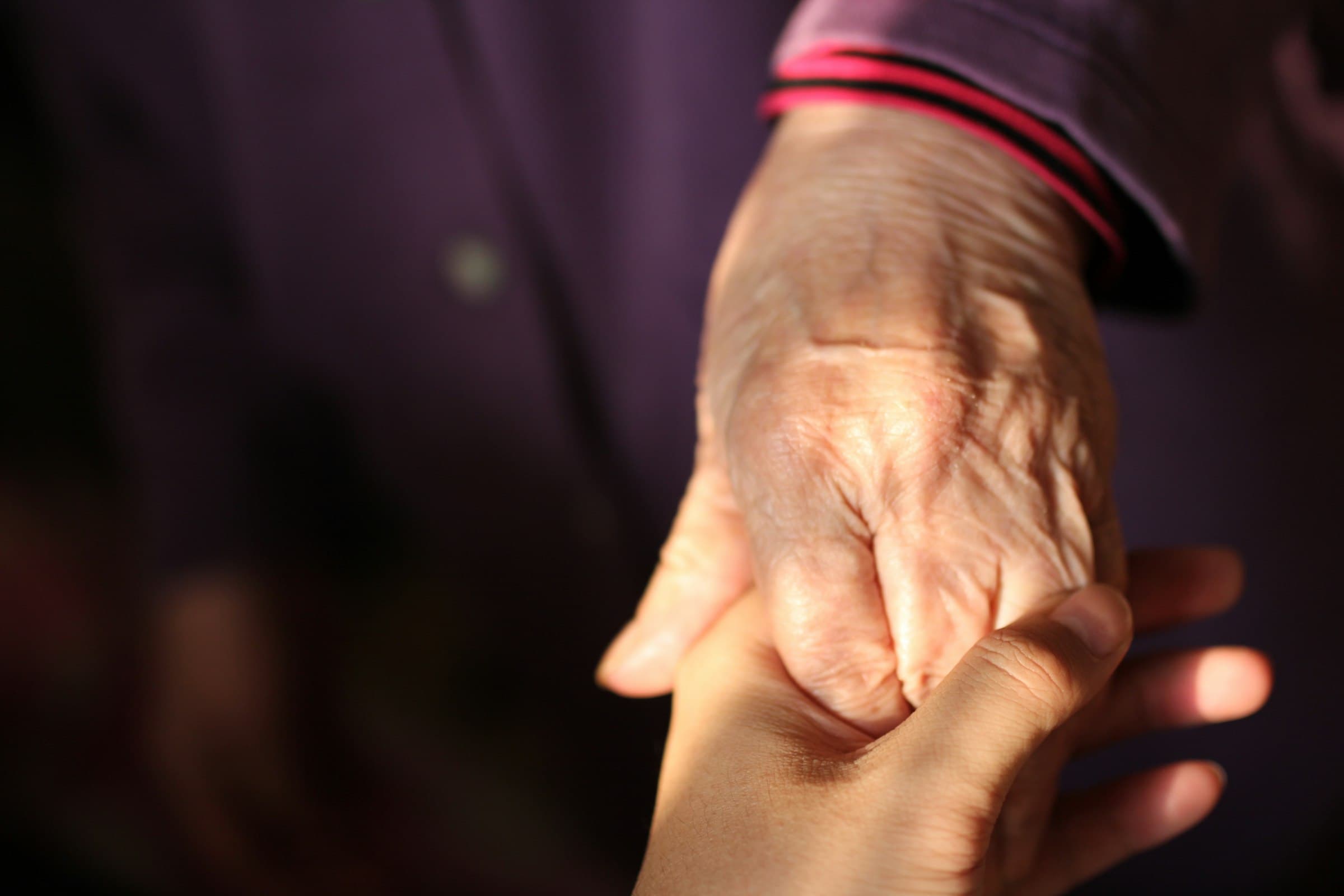 Two people holding hands, one older, in warm low light.