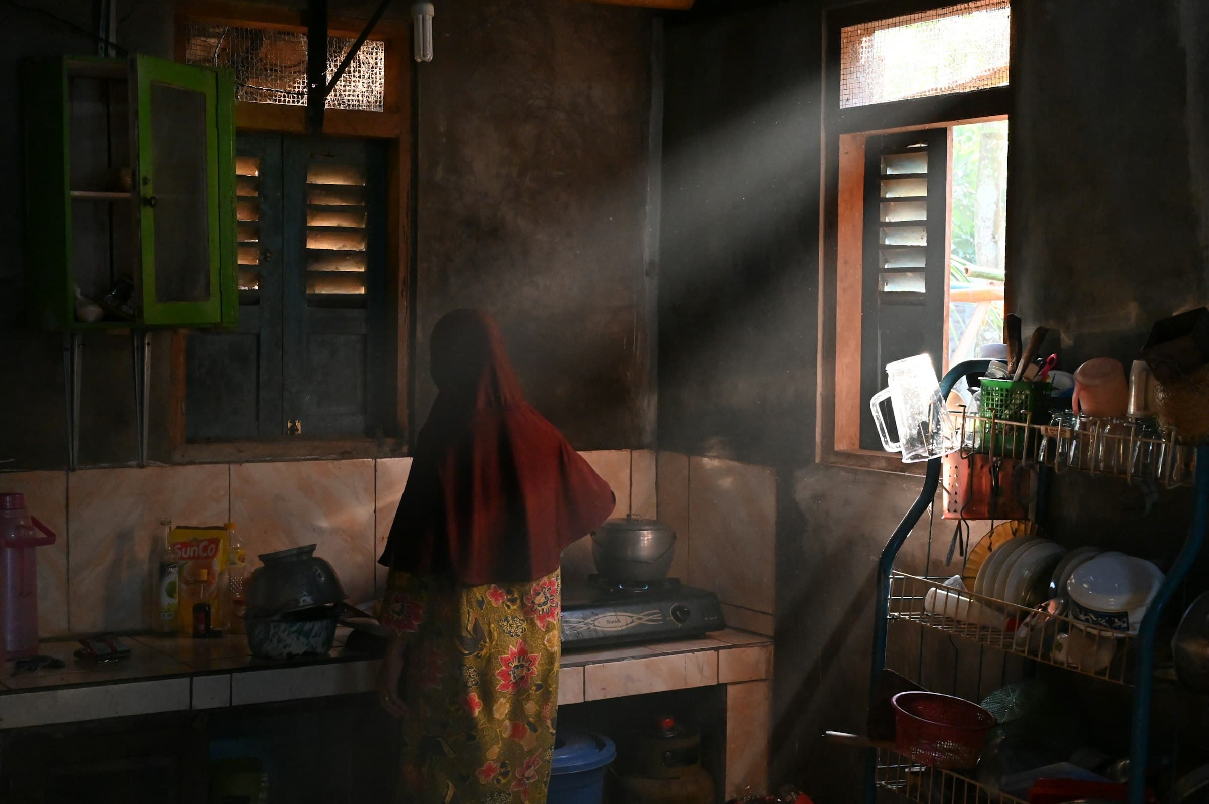 Morning light falling through a kitchen window onto a woman standing at the bench.