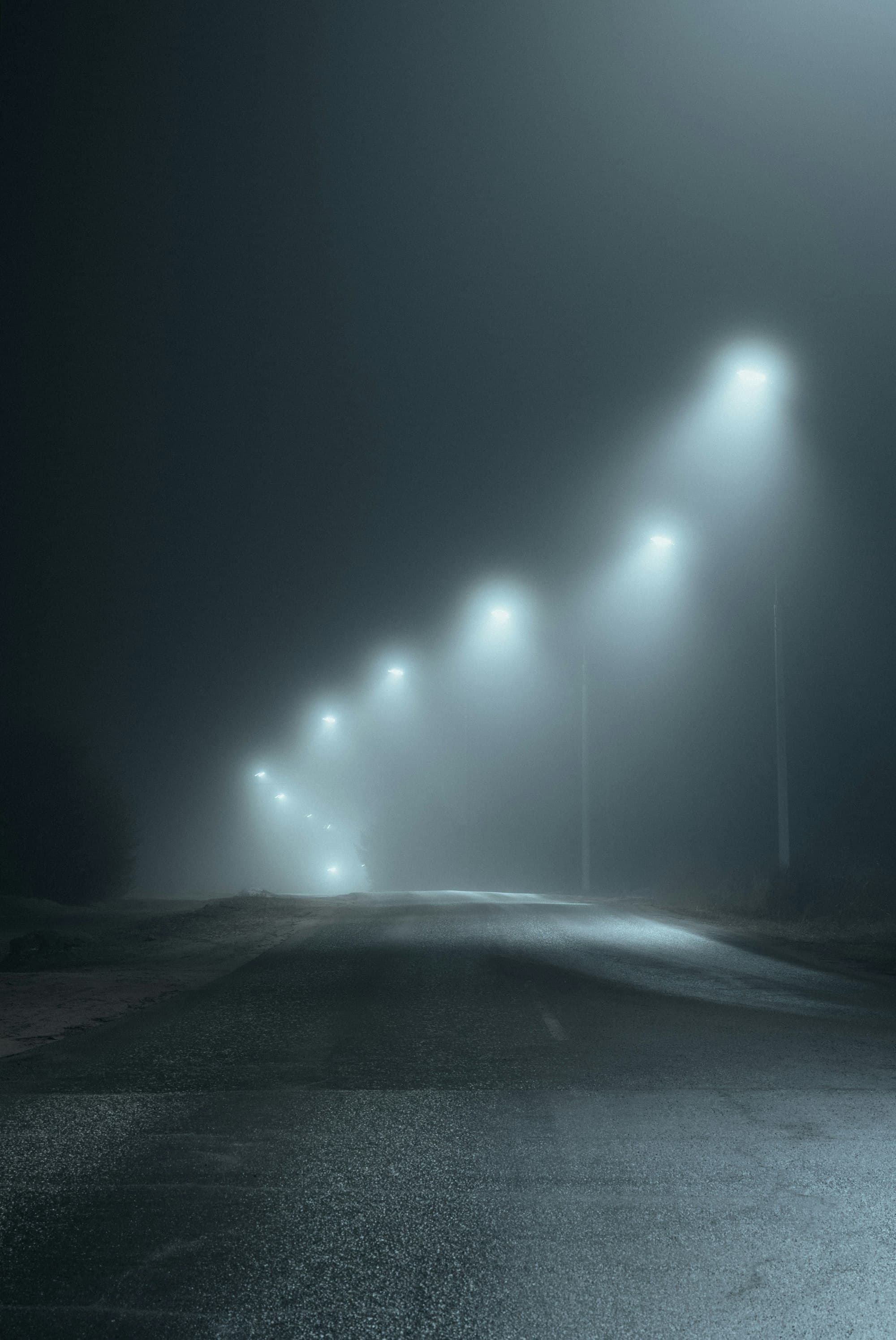 Street lights fading into fog along an empty road at night.