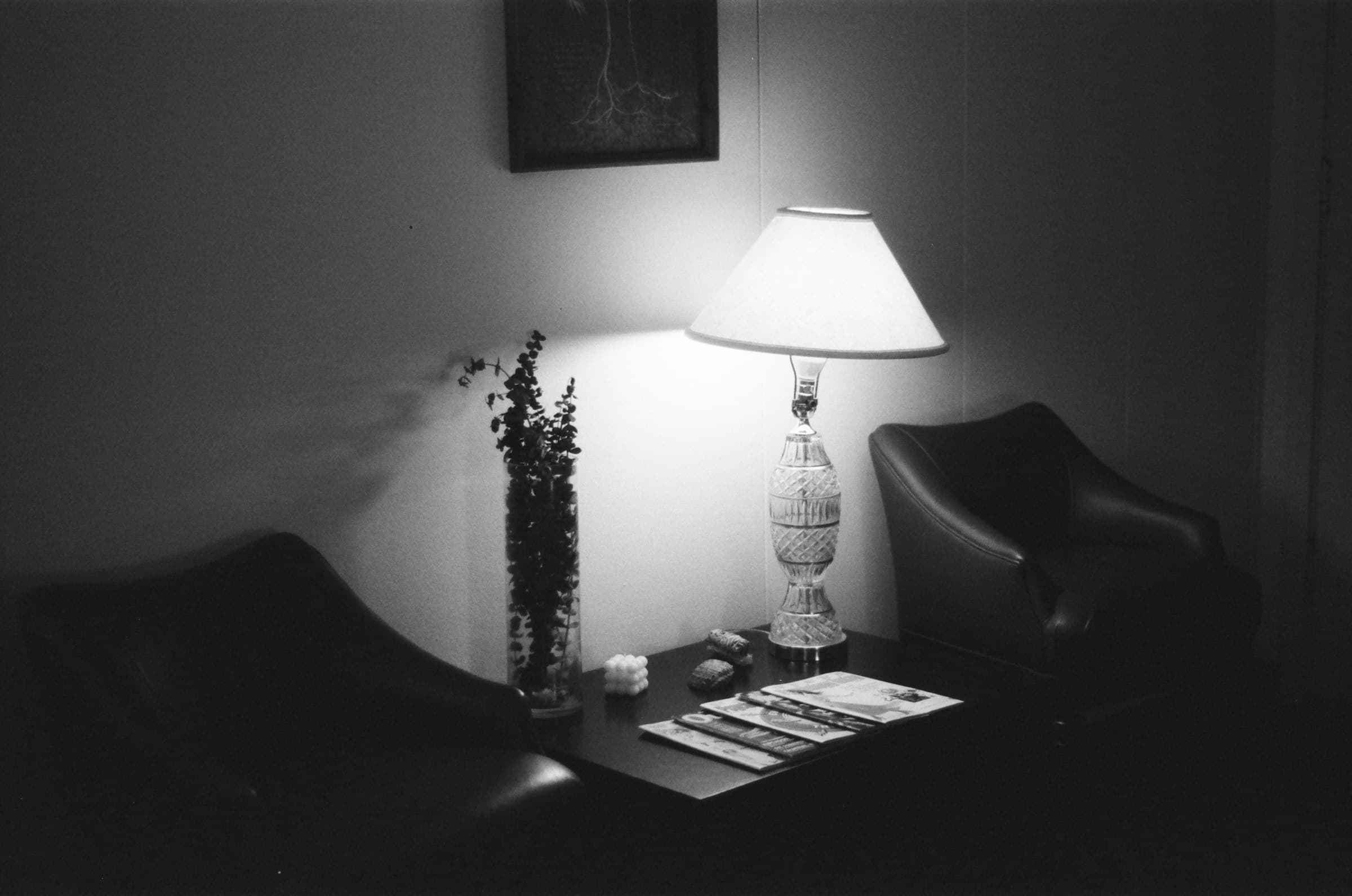 A dim waiting area: a table lamp, empty chairs and magazines.
