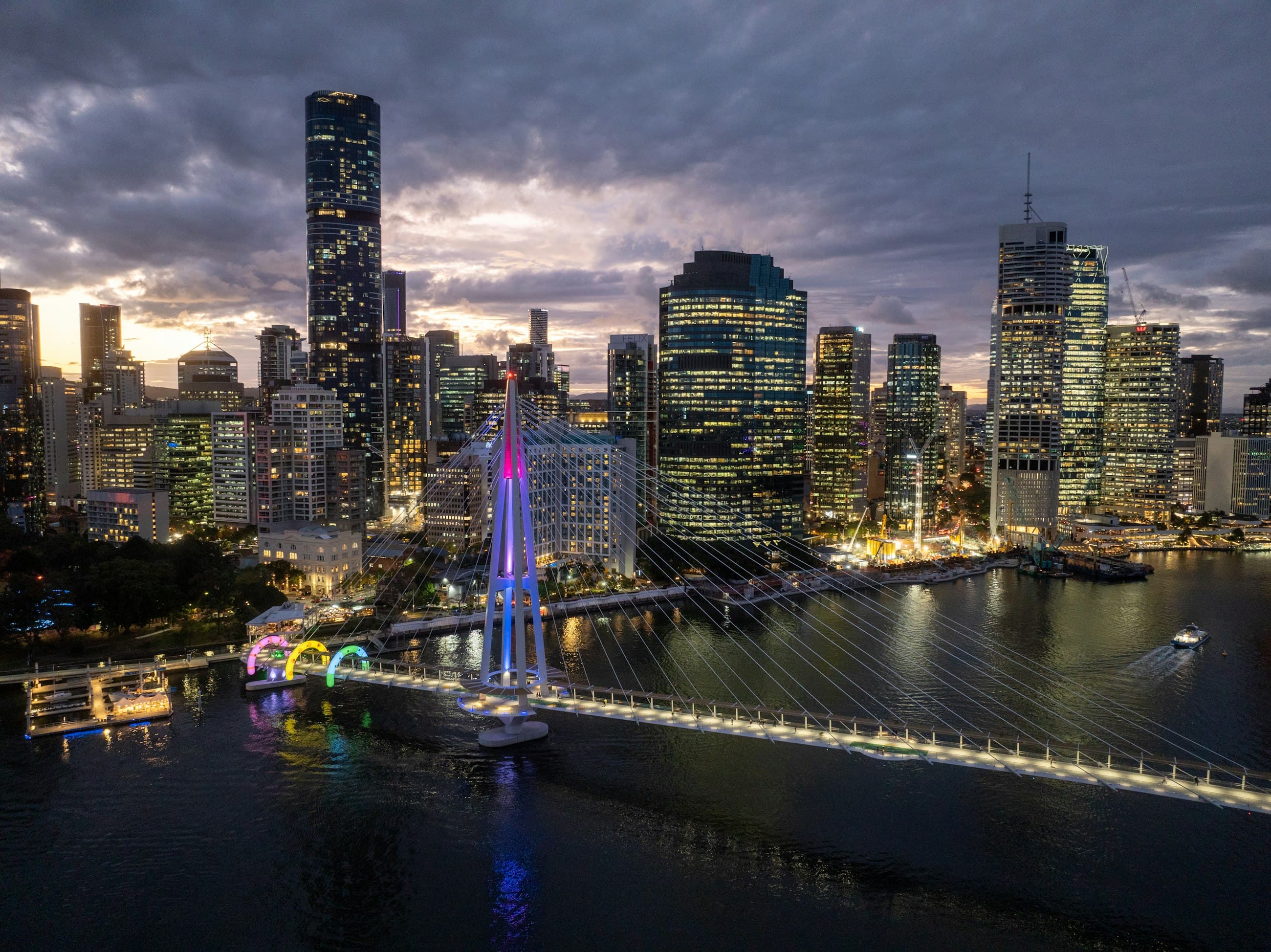 Brisbane at dusk, the city lit along the river beside a bridge.