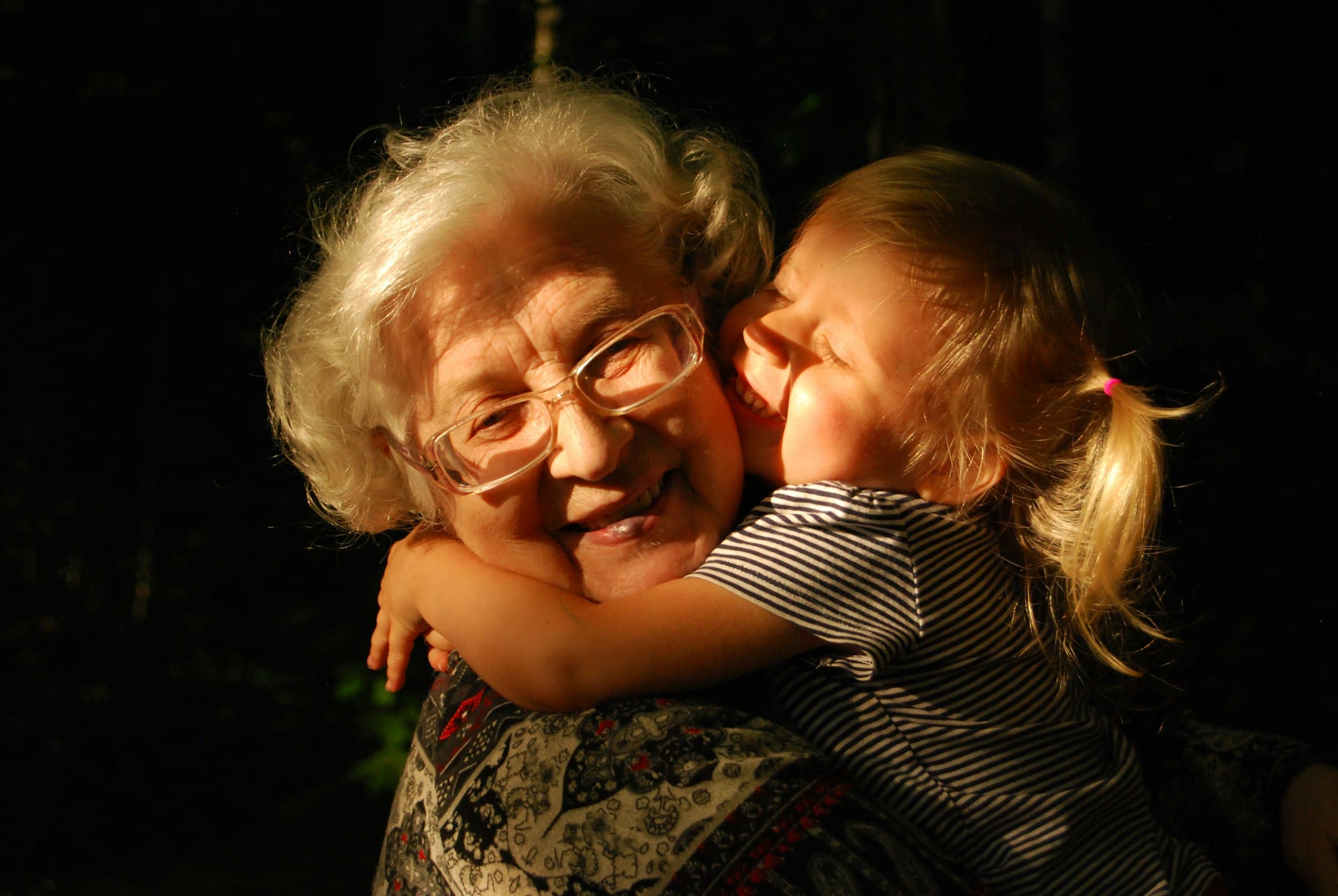 An older woman with white hair and glasses being hugged by a child.
