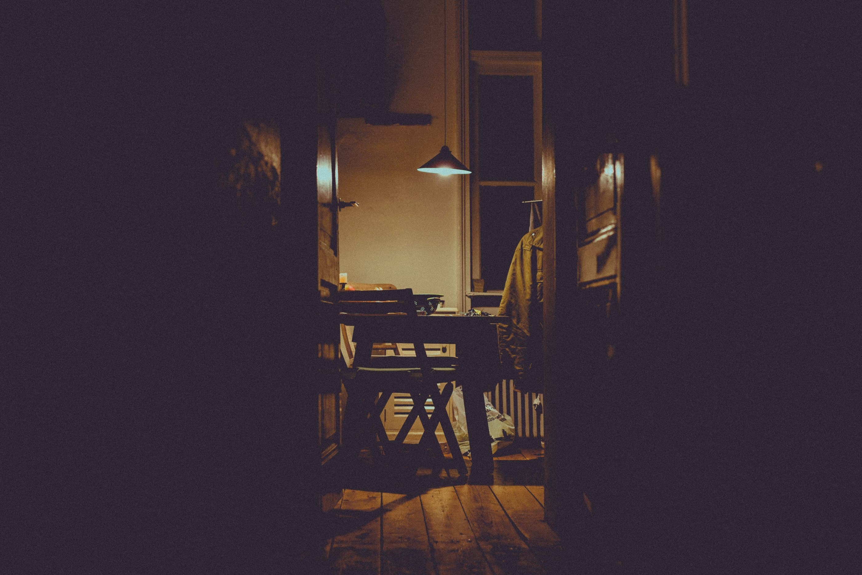 A doorway onto a kitchen at night, a single pendant lamp lit over the table.