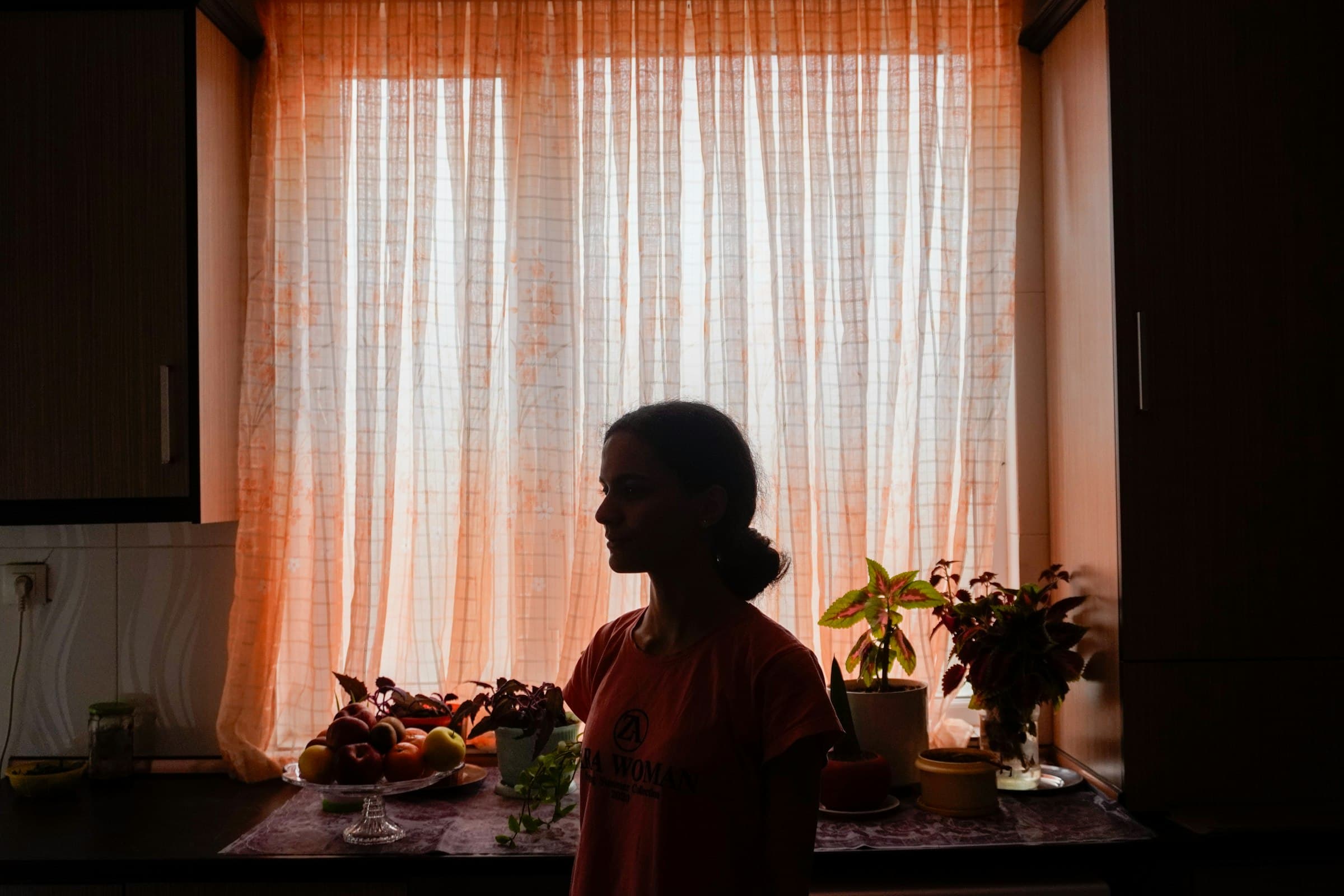 A woman in silhouette by a sunlit kitchen window.