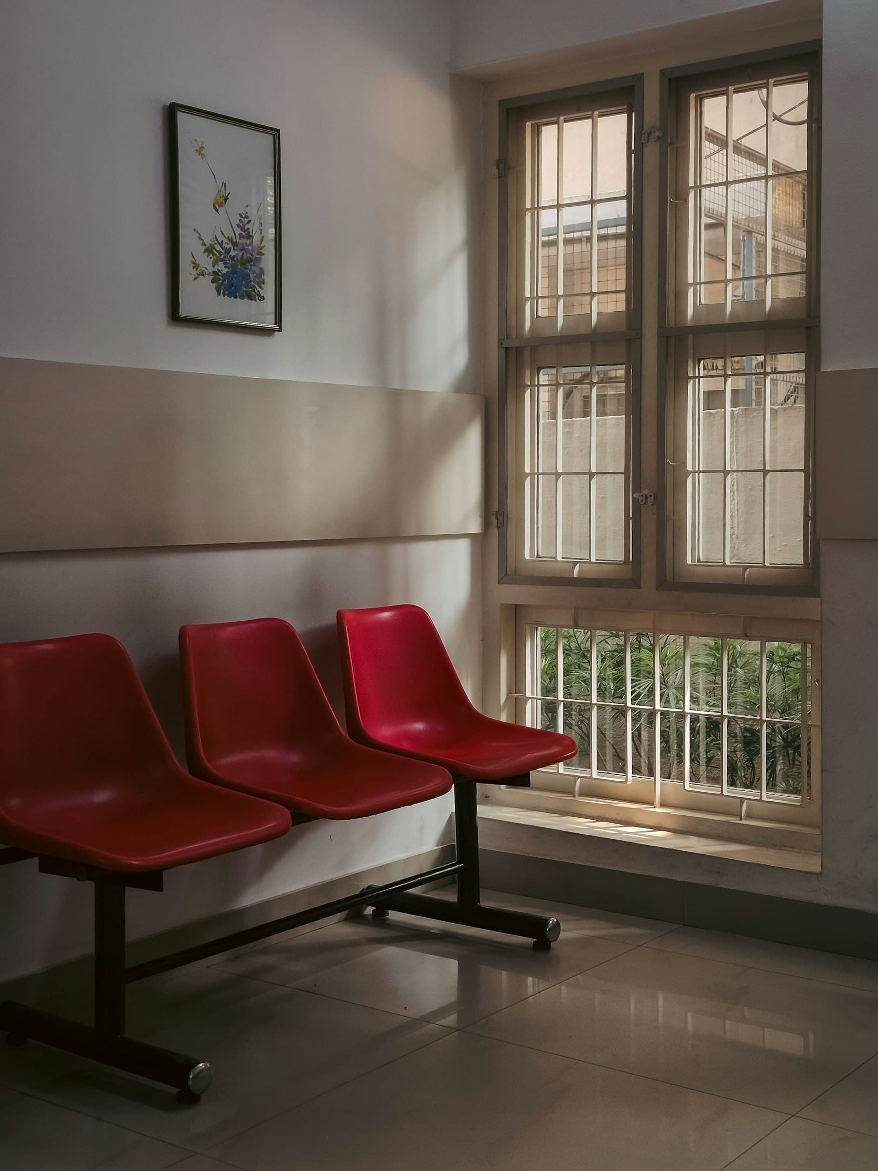 Three red chairs in an empty waiting room by a window.